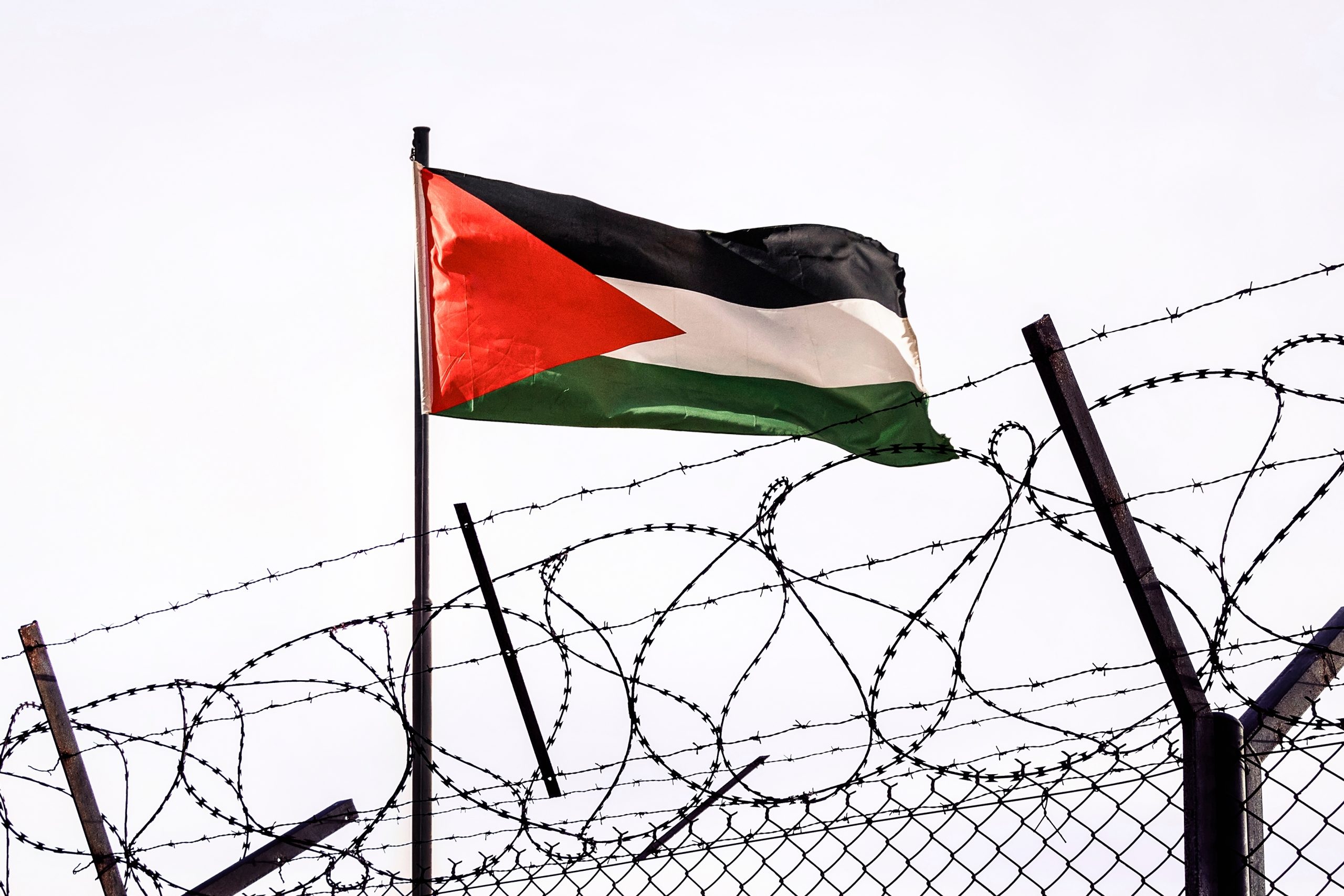 A Palestinian flag flies behind barbed wire.